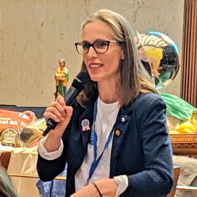 Juanita McClaren speaking at an event. She's wearing a blazer and has badges on her lapel such as the Aboriginal flag.